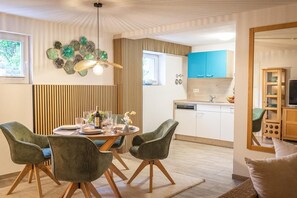 Eine moderne Küche mit weißen Schränken, einer blauen Arbeitsplatte und einem Essbereich mit einem runden Tisch und grünen Stühlen.