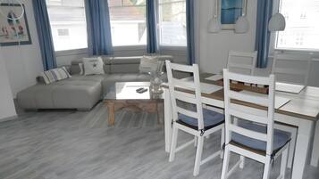 Ein modernes Wohnzimmer mit einer Eckcouch, einem Glastisch und weißen Stühlen.
