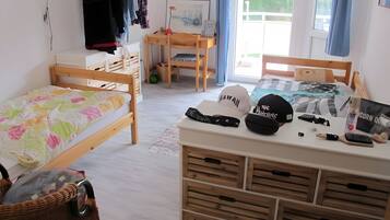 Ein Schlafzimmer mit zwei Holzbetten, einem Schreibtisch mit Stuhl, einem Fenster mit Vorhängen und verschiedenen Hüten auf dem Schreibtisch.