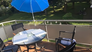 Ein Balkon mit Tisch und Stühlen, einem blauen Sonnenschirm und einem Fahrrad im Hintergrund.