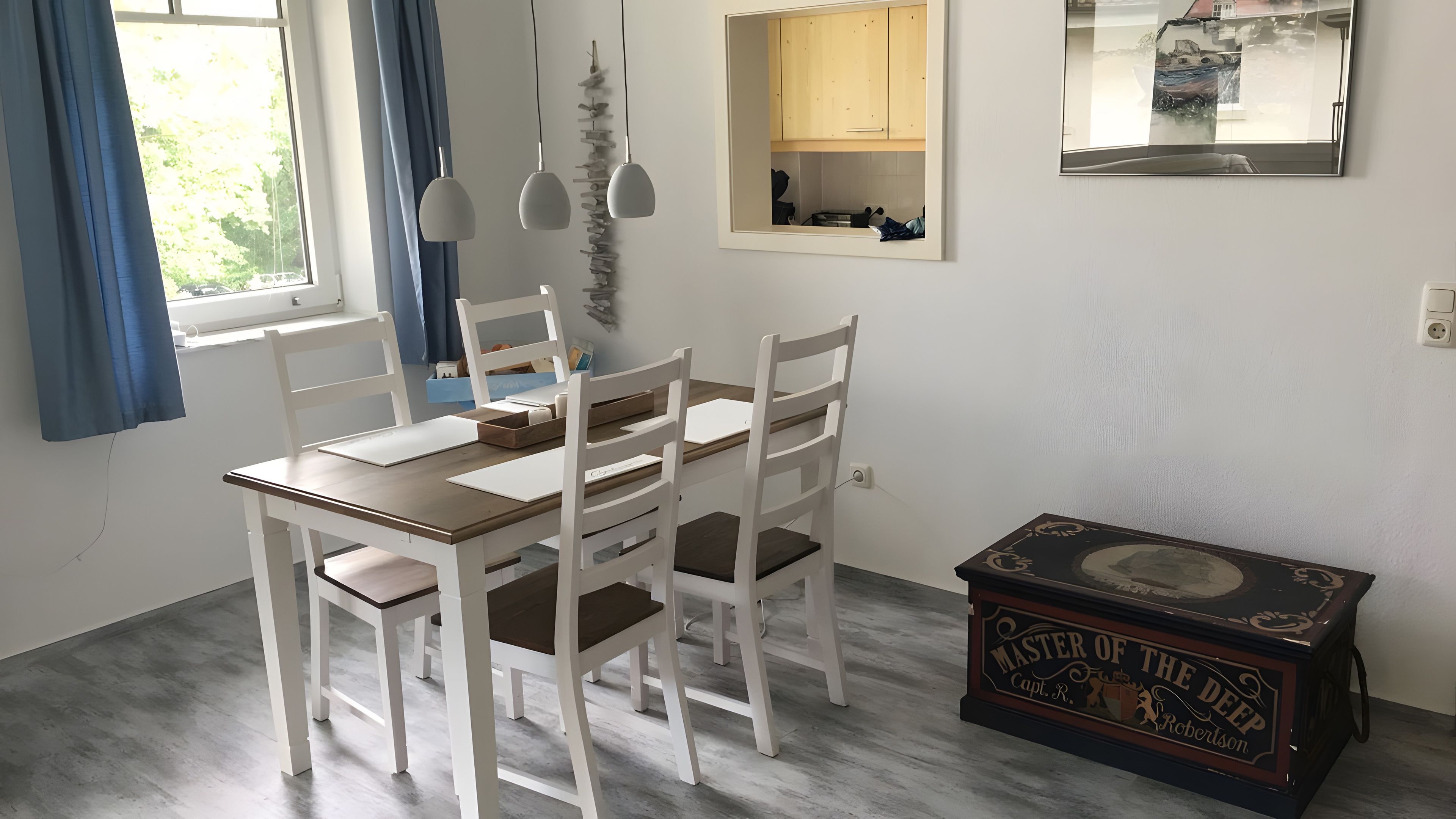 Ein Essbereich mit Holztisch und weißen Stühlen, einer kleinen Kommode, einem Spiegel und einer Zierkiste.