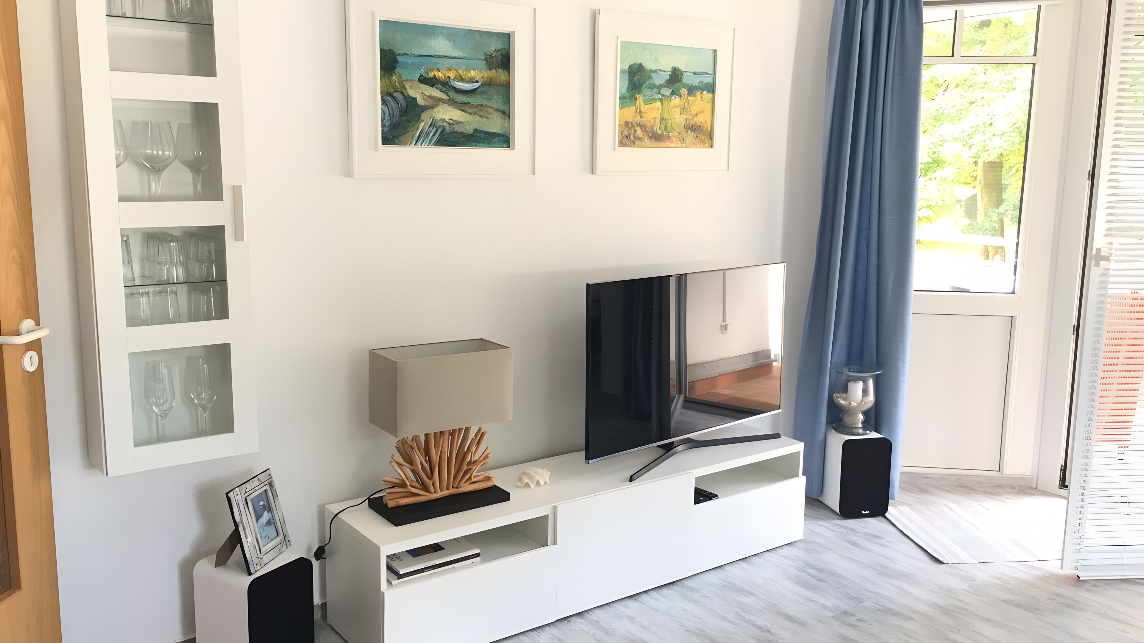 Ein modernes Wohnzimmer mit Flachbildfernseher, weißem Unterhaltungsschrank und gerahmten Kunstwerken an der Wand.