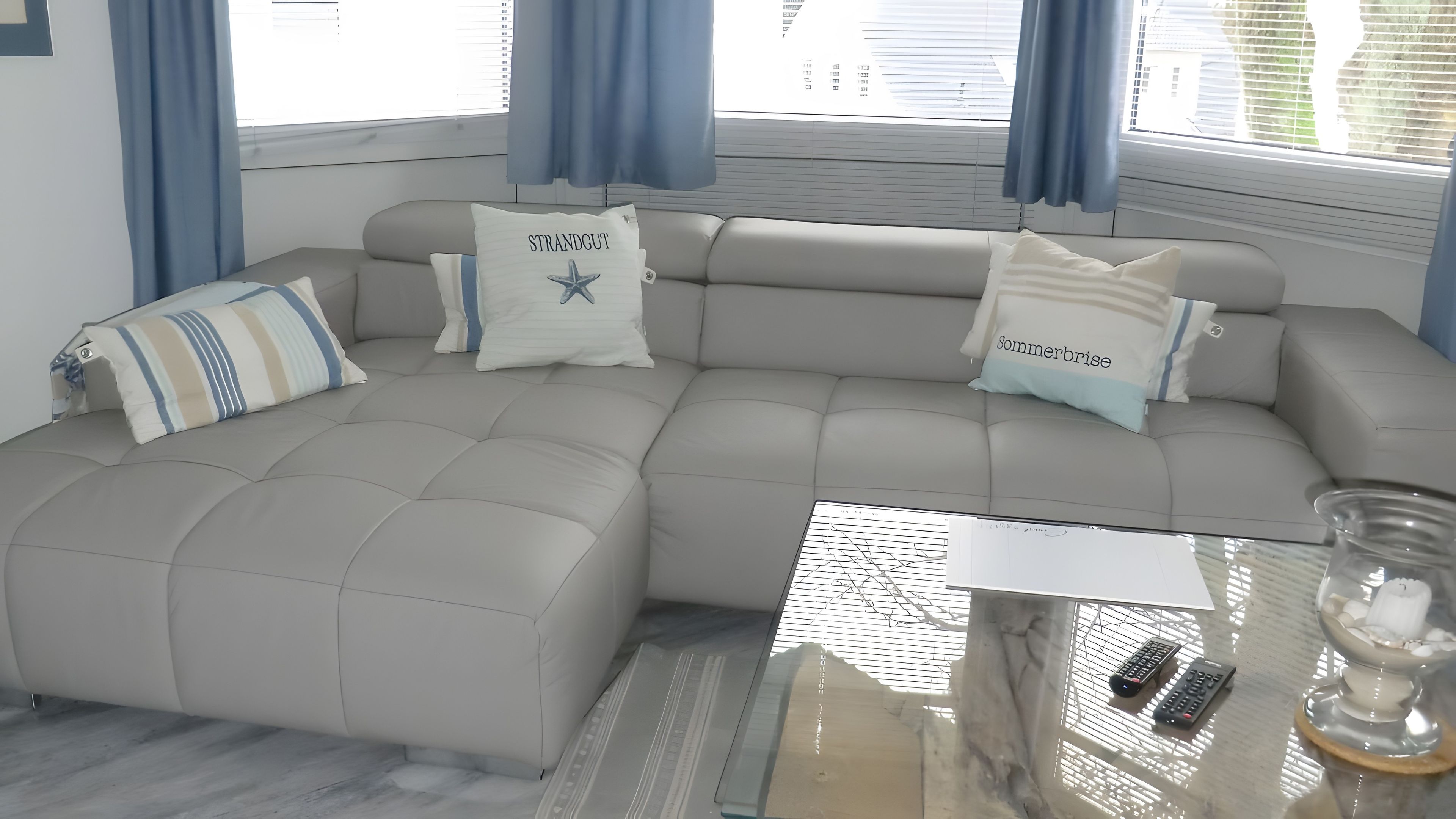 Ein modernes Wohnzimmer mit einem Ecksofa, einem Glastisch und dekorativen Kissen.