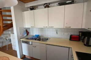 Eine kleine Küche mit weißen Schränken, einem Geschirrspüler, einer Spüle und einem Toaster.