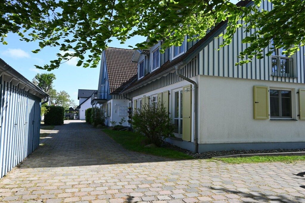 Ein schmaler Kopfsteinpflasterweg führt zu einer Reihe traditioneller Gebäude mit weißen Fassaden und blauen Akzenten.