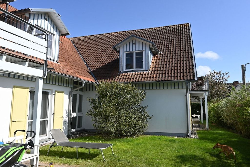 A residential property with a sloped roof, a small window, and a lawn with a chair and a dog.