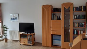 A living room with a television on a wooden stand, a bookshelf, and a radiator.