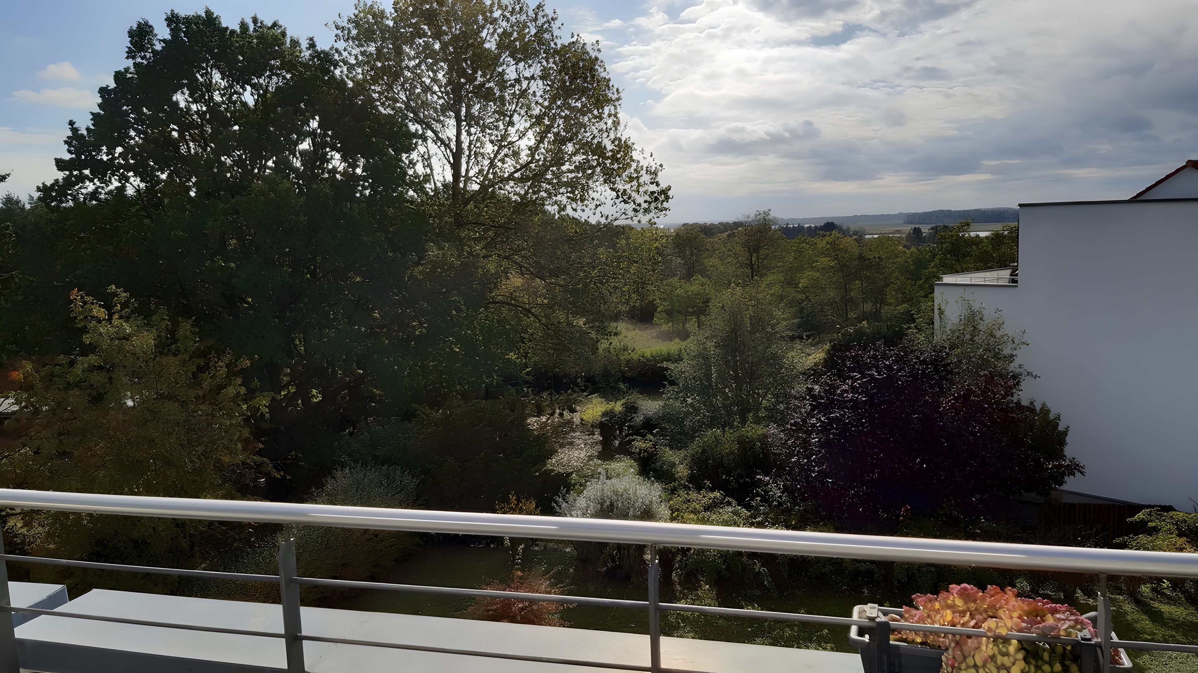 Ein Balkon mit Blick auf einen Garten und ein Gewässer.