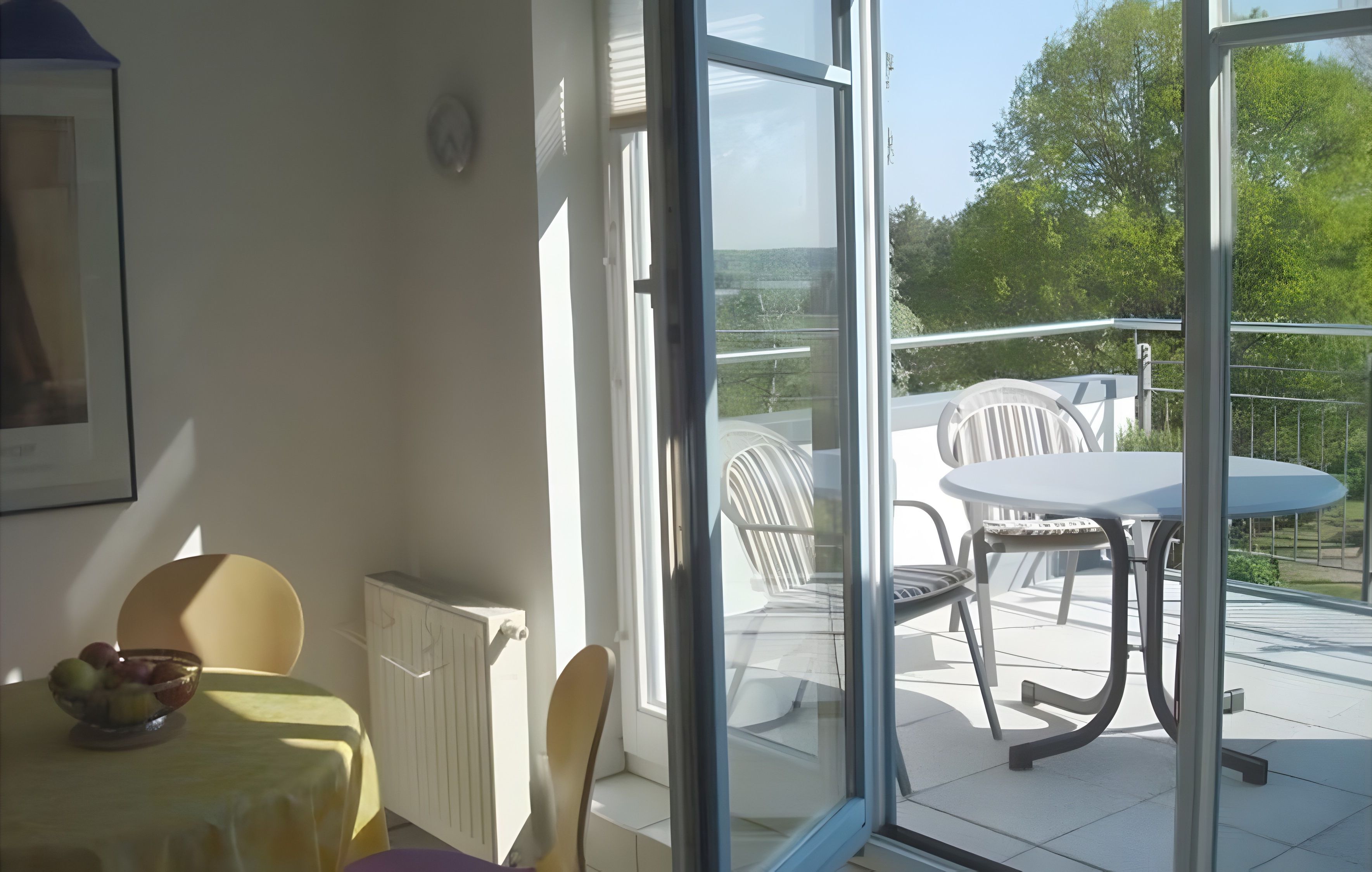 Ein Zimmer mit Tisch und Stühlen, einem Heizkörper und Blick auf einen Balkon mit Gartenmöbeln.