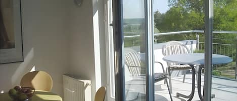 Una habitación con una mesa, sillas, un radiador y vistas a un balcón con mobiliario exterior.