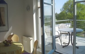 A room with a table and chairs, a radiator, and a view of a balcony with outdoor furniture.