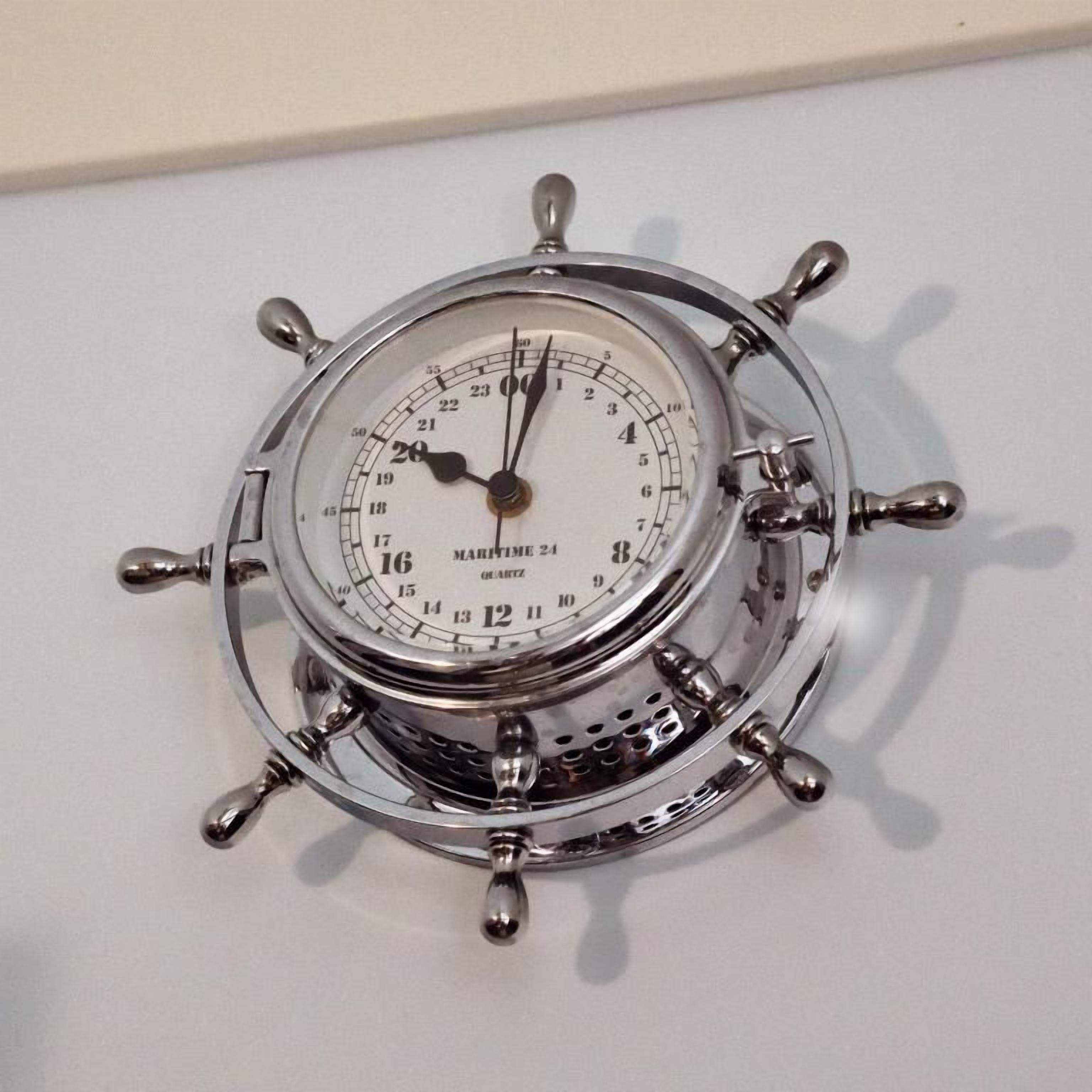 Orologio da parete in stile nautico con motivo della ruota di una nave, dotato di lancette per le ore e i minuti e un quadrante centrale con numeri.