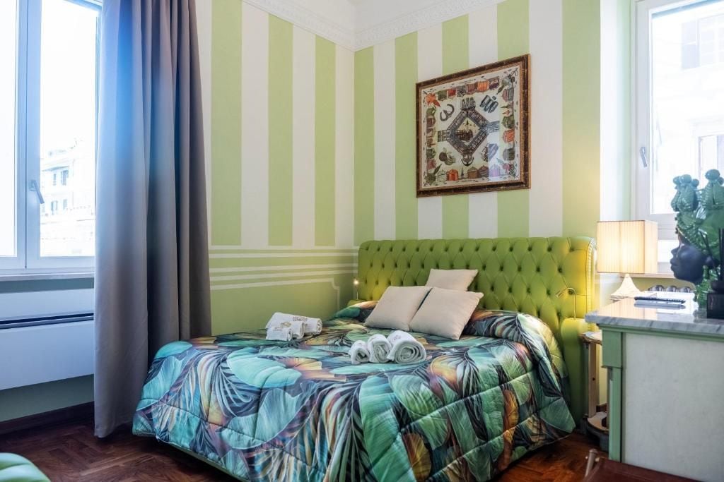 A hotel room with a bed, a window with curtains, a framed picture on the wall, and a lamp on a side table.