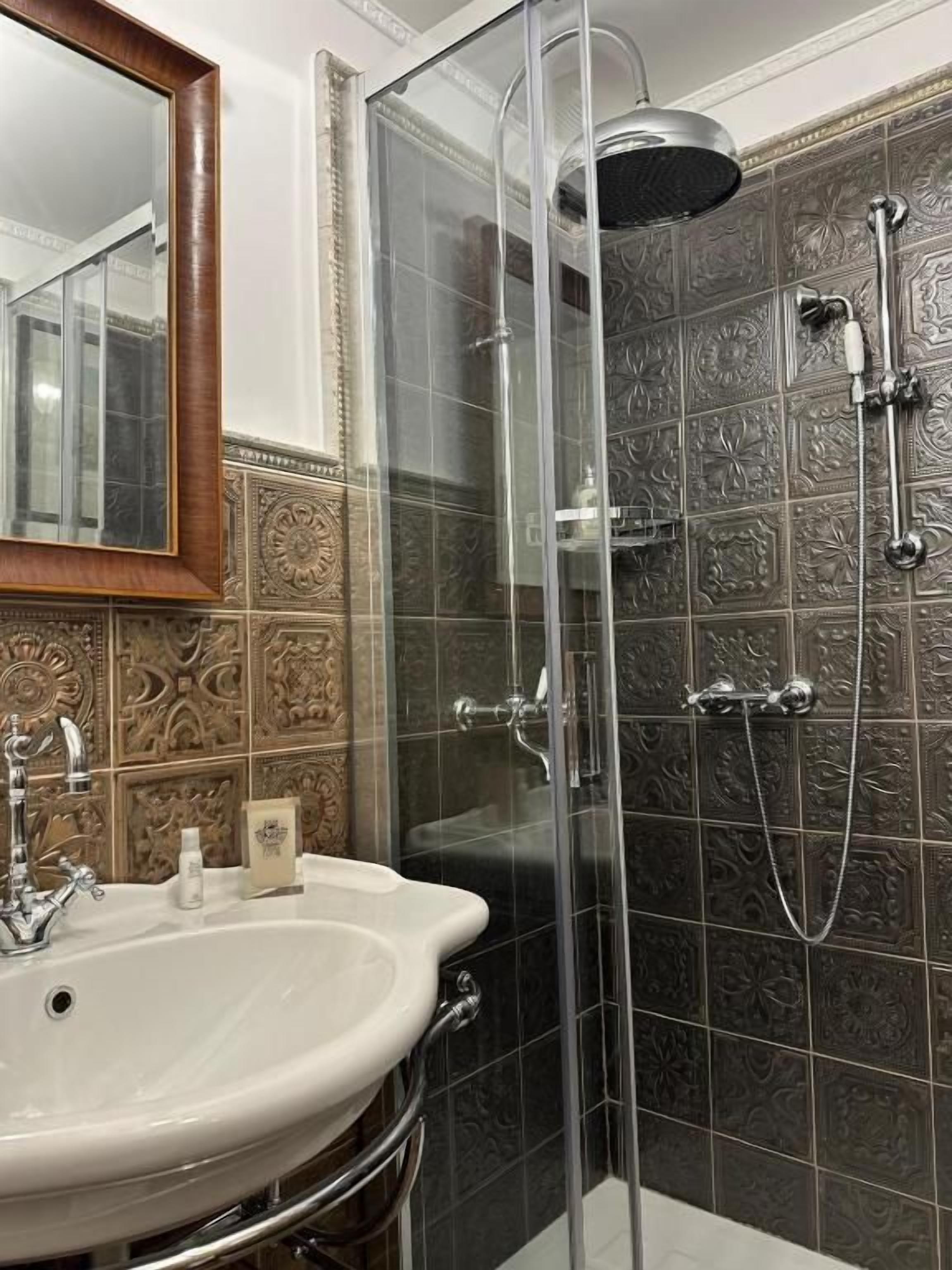 A bathroom with a glass-enclosed shower, a sink, and ornate wall tiles.
