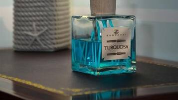 En flaske 'Turquoise' cologne med rørreder på et bord, en lampe og en flettet kurv i baggrunden.