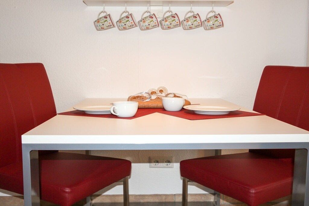 Mesa de jantar com duas cadeiras, pratos, xícaras e uma cesta de pão.