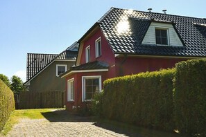 Ein rotes Haus mit geneigtem Dach und Schornstein, einer gepflasterten Auffahrt und einem Holzzaun.