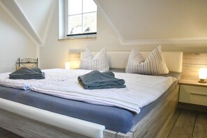 Ein Schlafzimmer mit einem Bett, Kissen, einem Nachttisch mit Lampe und einem Fenster mit Blick zum Himmel.