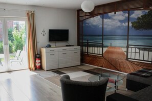 A modern living room with a large window offering a view of the sea, a flat-screen TV, and a glass coffee table. - Swan in the house at the sweetling (Glowe)