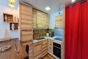 A compact kitchen with wooden cabinets, a sink, a stove, and a red curtain. - 2-Bedroom Apartment in Les Deux Alpes (Les Deux Alpes)