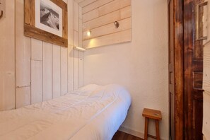 Una cama individual en una habitación con paredes de madera y un pequeño taburete de madera.