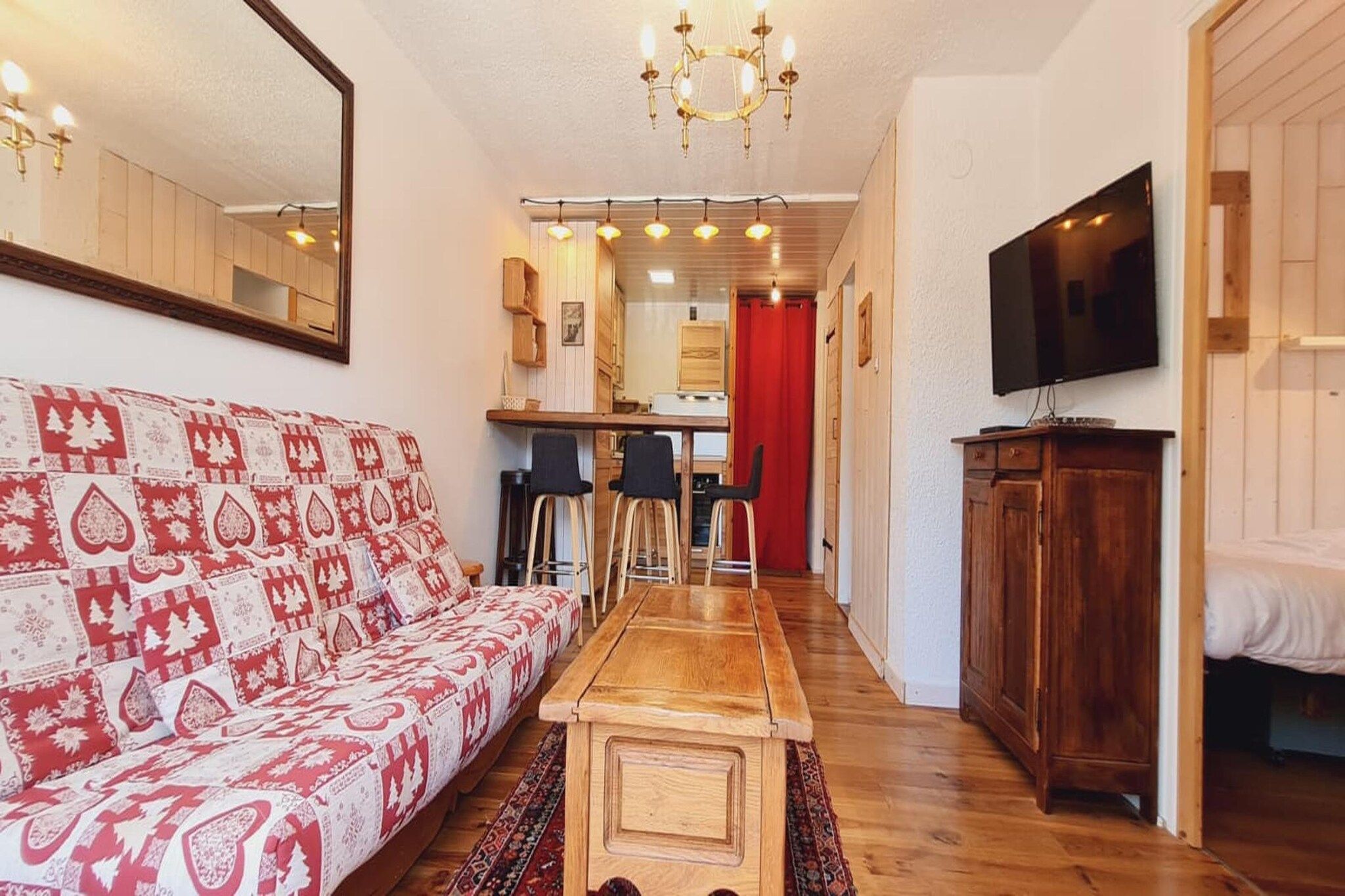 A cozy living room with a patterned sofa, a wooden coffee table, and a television on the wall.