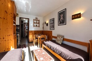 Ein gemütliches Zimmer mit einer hölzernen Bank, einem Tisch und einem Bett. Eine Wandhalterung trägt dekorative Gegenstände und ein gerahmtes Bild.