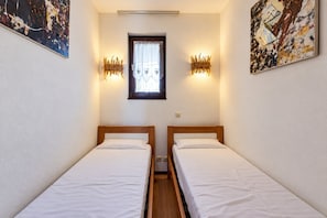 Ein kleines, sauberes Zimmer mit zwei Einzelbetten, einem Fenster mit Vorhang und Wandleuchten.