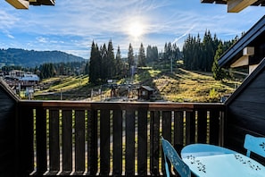 Ein hölzerner Balkon mit Blick auf eine gebirgige Landschaft, ein Stuhl und ein Tisch.