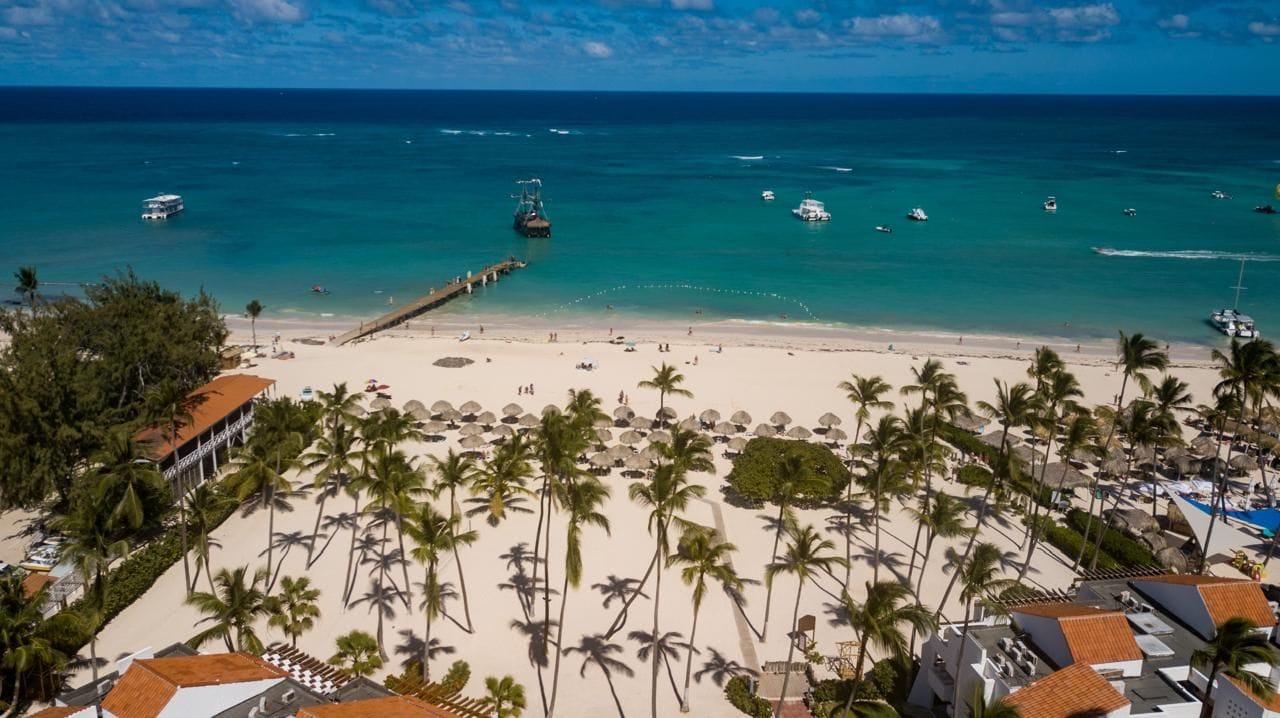 A beach with palm trees, a pier, and boats in the water.