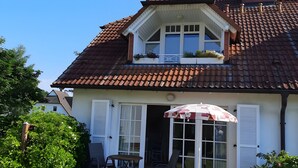 Ein zweistöckiges Gebäude mit einem Ziegeldach, weißen Fensterläden und einem Balkon mit Blumentöpfen.