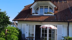 Ein zweistöckiges Gebäude mit einem Ziegeldach, weißen Fensterläden und einem Balkon mit Blumentöpfen.