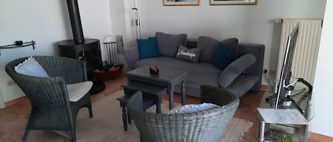 Een zithoek met een bank, twee rieten stoelen, een salontafel, een open haard en een radiator.