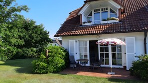 A house with a tiled roof, a front door, and a small patio with a table and chairs. - Apartment 'Zempin Seebad, Dorfstraße 20' with Wi-Fi (Zempin (Seebad))