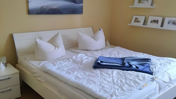 A neatly made bed with white bedding and pillows, a bedside table with a lamp, and a wall with framed pictures.