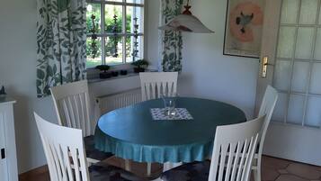 A dining area with a round table, white chairs, a teal tablecloth, and a hanging light fixture.