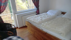 A bedroom with a wooden bed, a chair, and a window with curtains. - Apartment "Koserow Seebad, Waldstraße 14" with Balcony and Wi-Fi (Koserow)