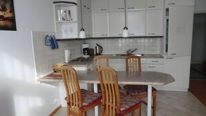 Een keuken met witte kasten, een eettafel en vier houten stoelen met gestreepte kussens.