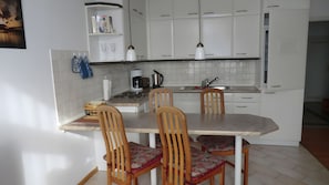 A kitchen with white cabinets, a dining table, and four wooden chairs with patterned cushions. - Apartment "Koserow Seebad, Waldstraße 14" with Balcony and Wi-Fi (Koserow)