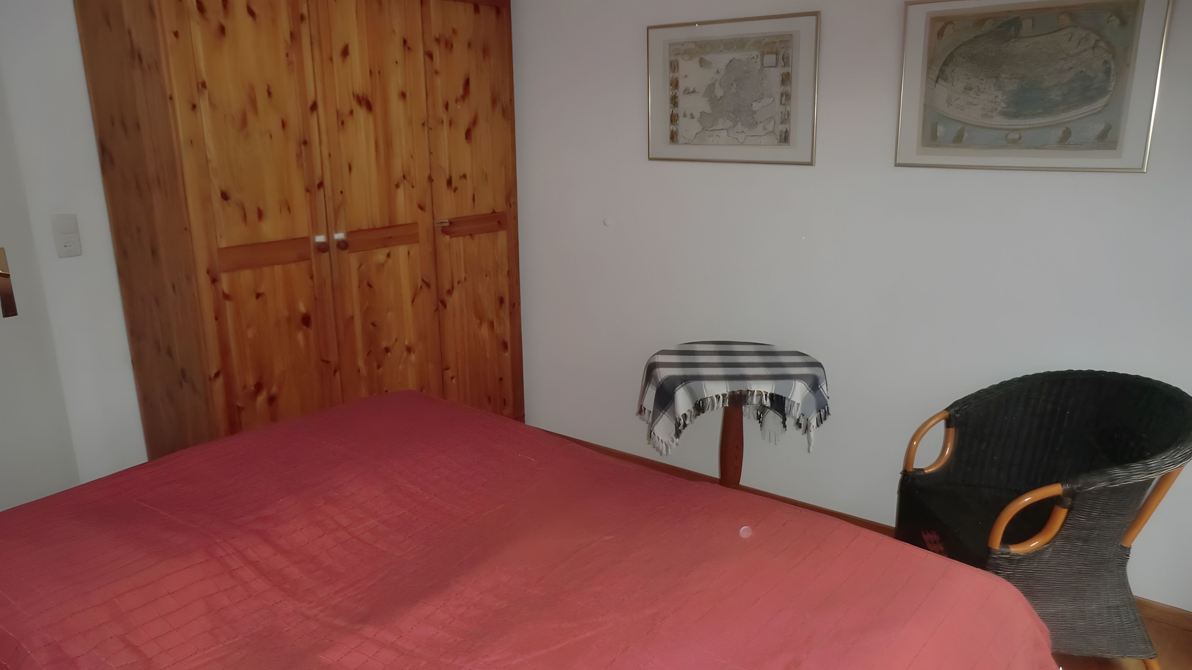 Ein Zimmer mit einem Bett, einem Holzschrank, einem kleinen Tisch mit einer Tischdecke und einem Stuhl.