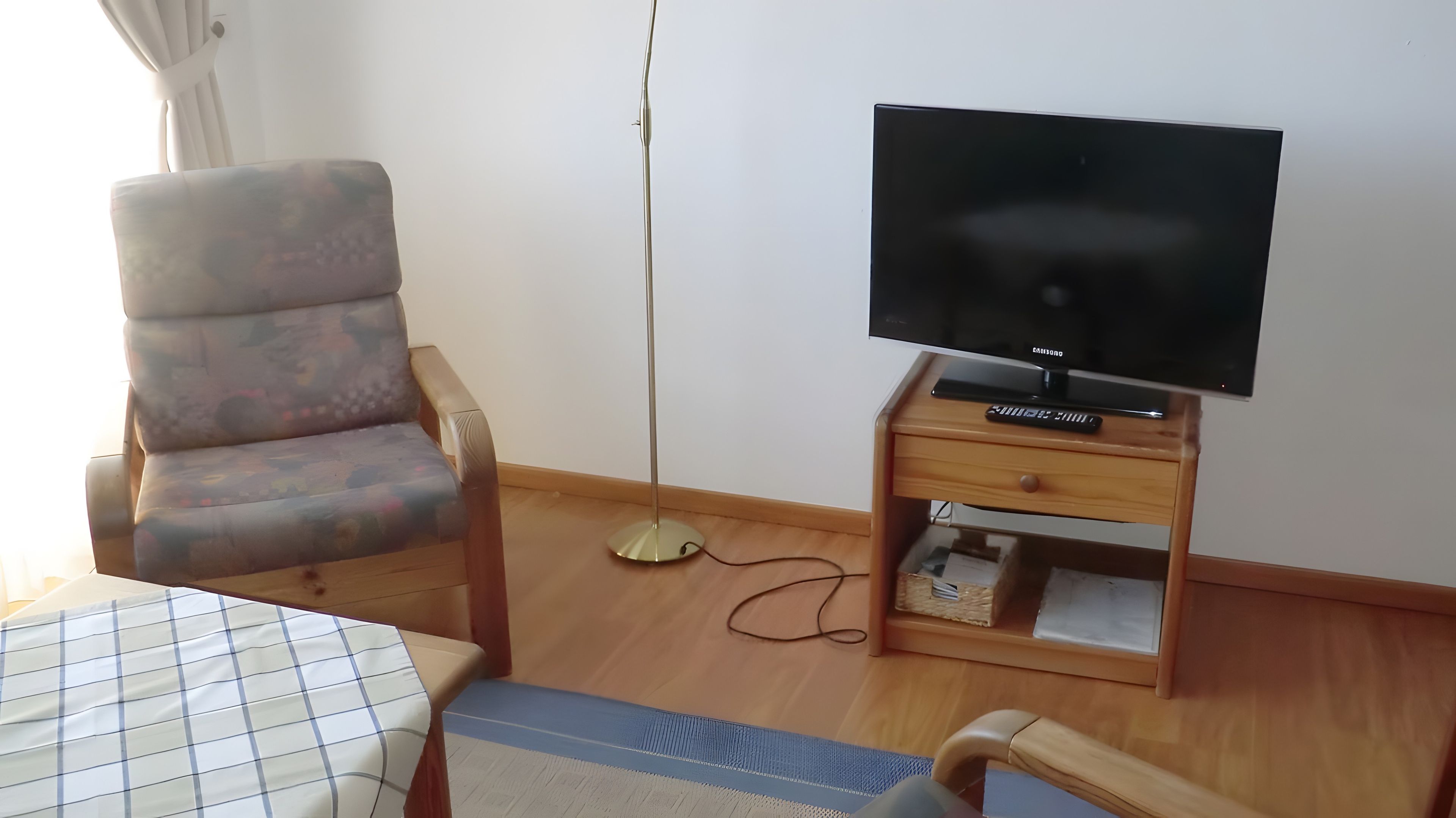 Een kamer met een bank, een televisie op een houten dressoir, een vloerlamp en een bed met een gestreept dekbed.