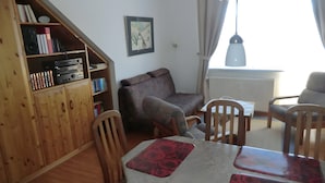 Een gezellige zithoek met een houten boekenkast, een bank, een eettafel en stoelen.