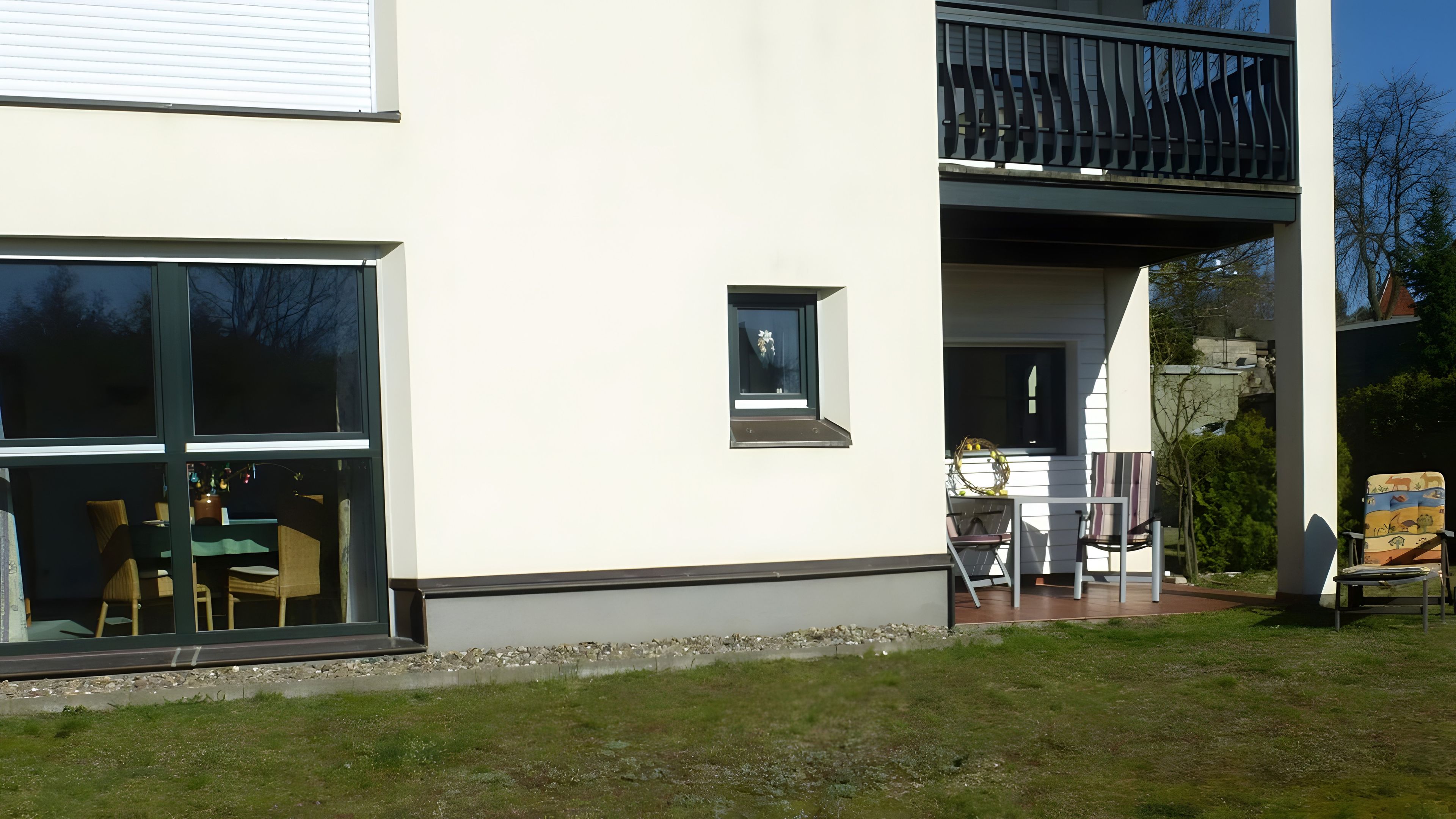 A modern house with a balcony, a dining area with outdoor furniture, and a small window.