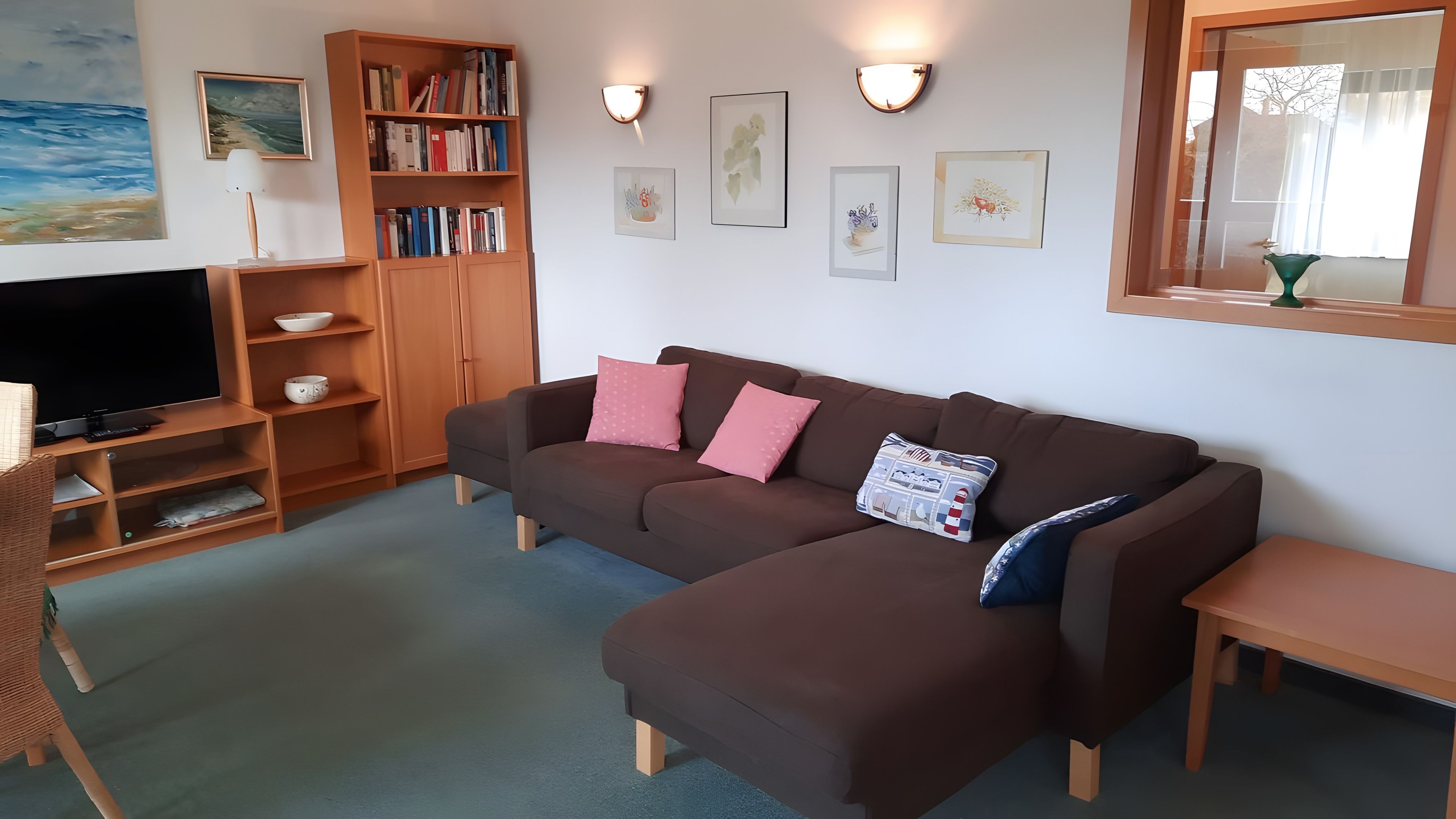 Een woonkamer met een bruine bank, een televisie, een boekenkast en lijstwerken aan de wanden.