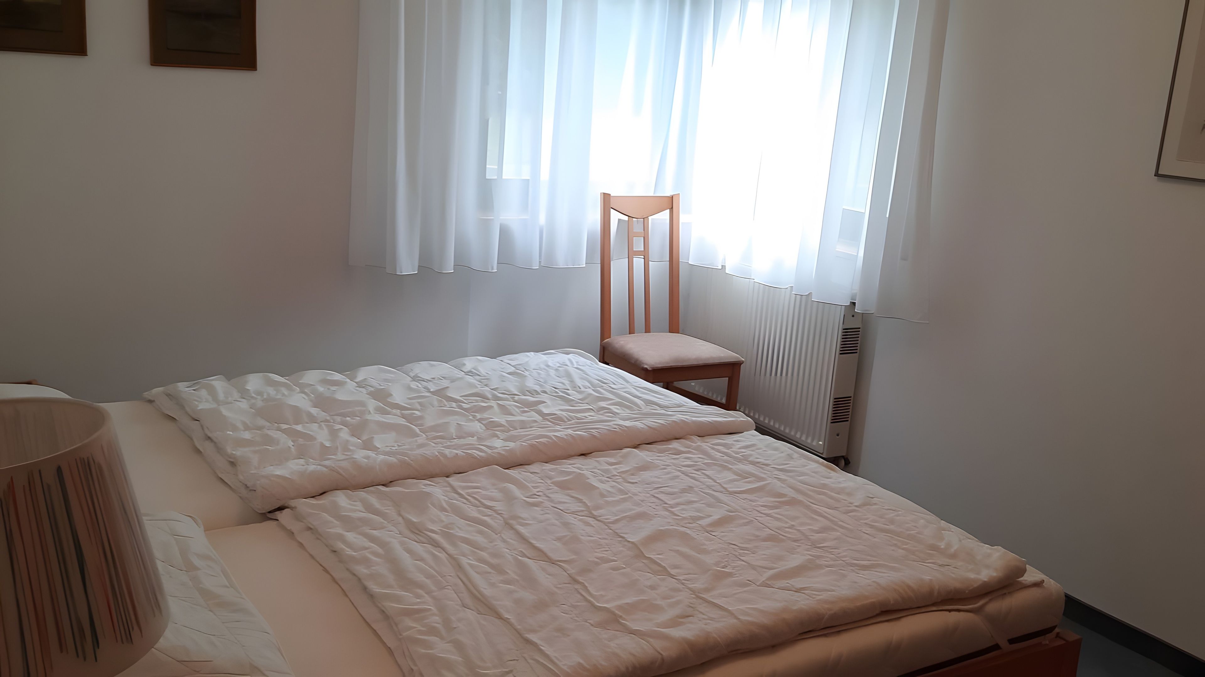 A bedroom with a bed, a chair, a bedside table, and a window with curtains.