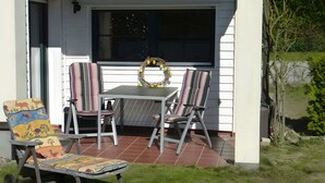 Een terras met een tafel en stoelen, een decoratieve krans op het raam, en een kleurrijke stoel met dierenprint.