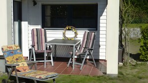 A patio with a table and chairs, a decorative wreath on the window, and a colorful chair with animal prints. - Apartment "Koserow Seebad, Lindenstraße 18" with Private Terrace, Garden & Wi-Fi (Koserow (Seebad))