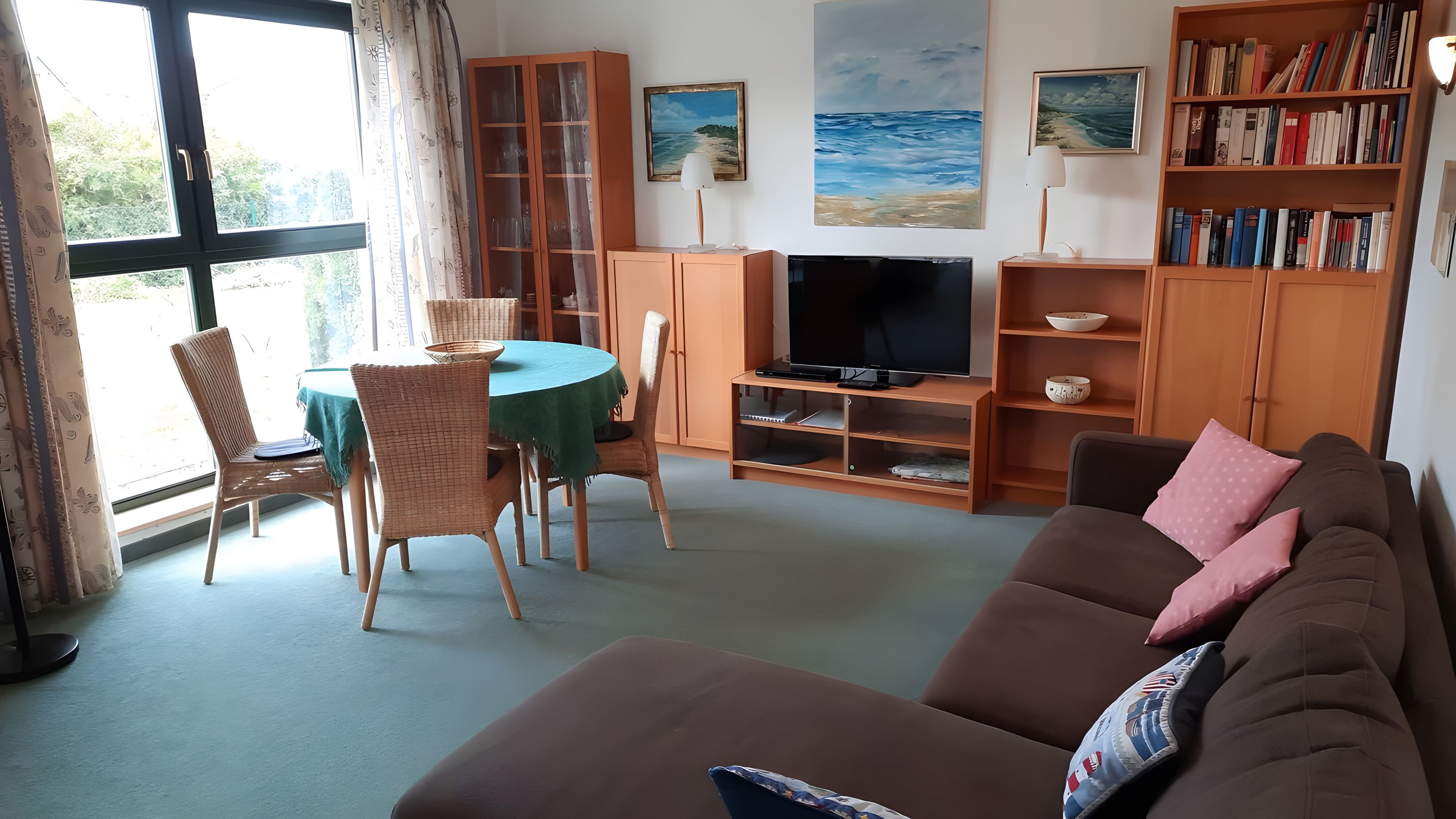 Una sala de estar con televisor, un sofá, una mesa de comedor con sillas y una estantería.