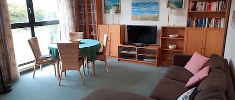 A living room with a television, a sofa, a dining table with chairs, and a bookshelf.