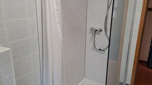 Een douchecel met een glazen deur, witte betegelde wanden en een douchekop aan de muur.